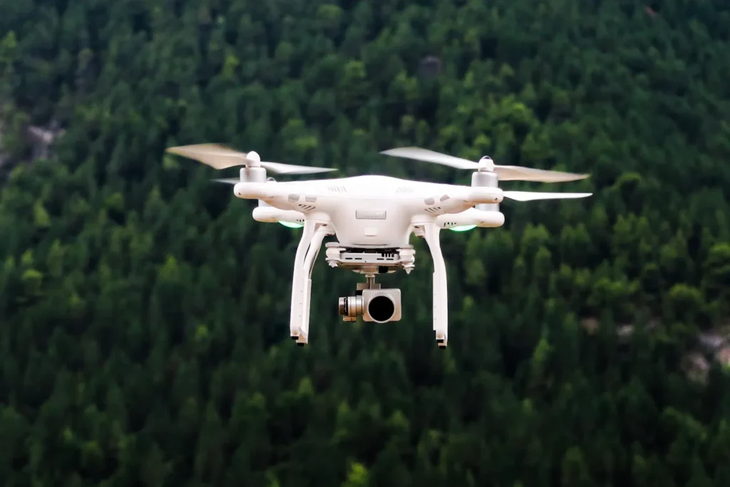 White quadcopter drone in flight over a forest