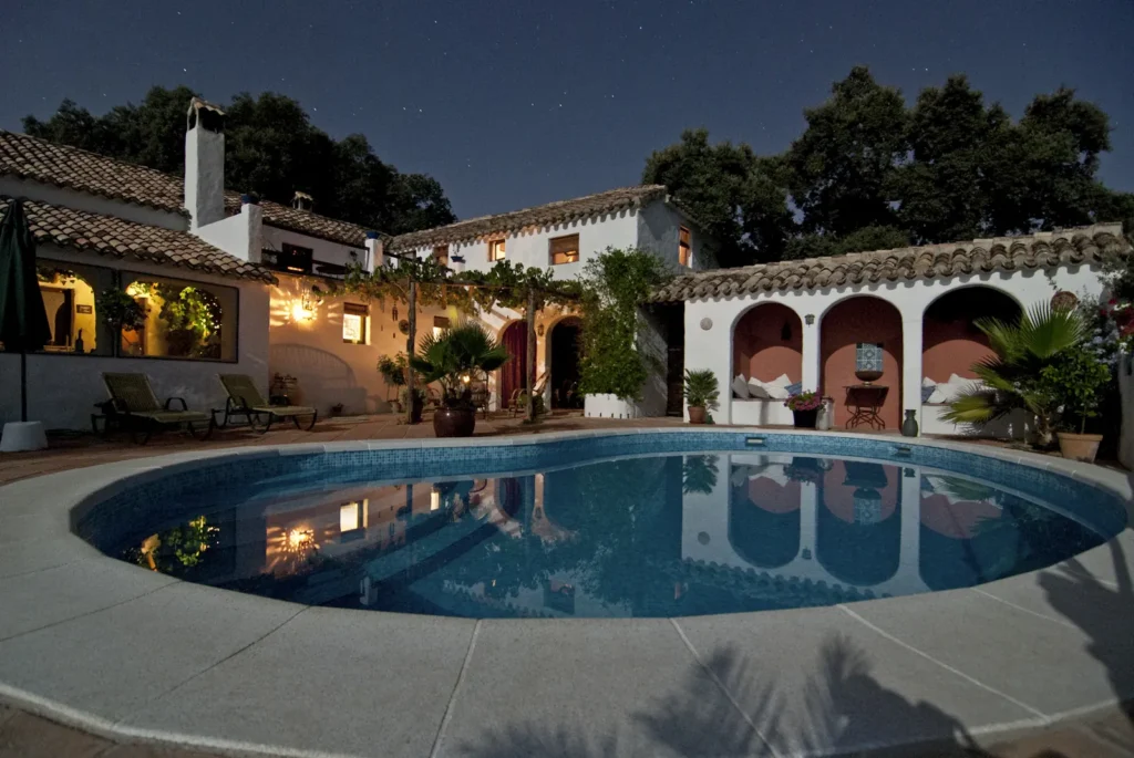 Lit backyard swimming pool beside a large home at dusk