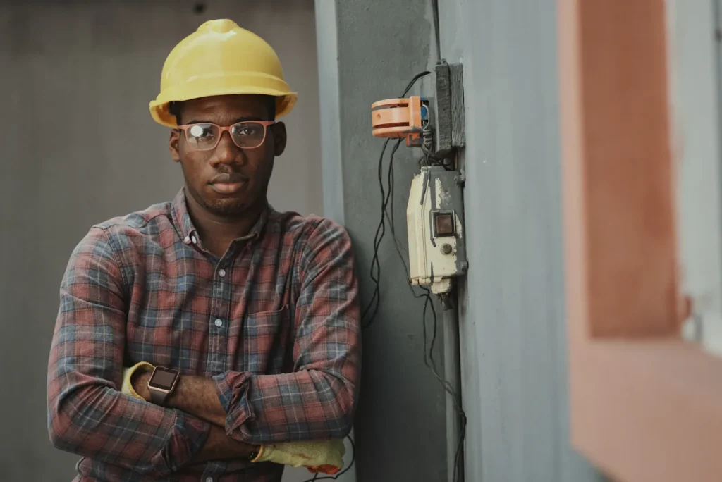 Technician in a hard hat standing beside an electrical panel
